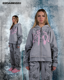 Grey/Pink Split Zip Jacket from 22DABE22: A long sleeve hooded zip jacket with a unique split design in grey and pink. Front features screen print and embroidery appliqué, with screen print on sleeves. Special feature zipper at the back allows for reversible wear. Made from 80% cotton and 20% polyester, weighing 500 GSM. Soft peached finish on the inside, with a distressed finish for edginess.