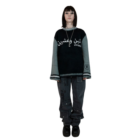 A pair of grey denim jeans with a long cut design and glitter print on the right leg. The jeans feature custom button and rivets, six usable pockets at the front, and an oversized unisex fit. Perfect for stacking on shoes for an on-trend look.