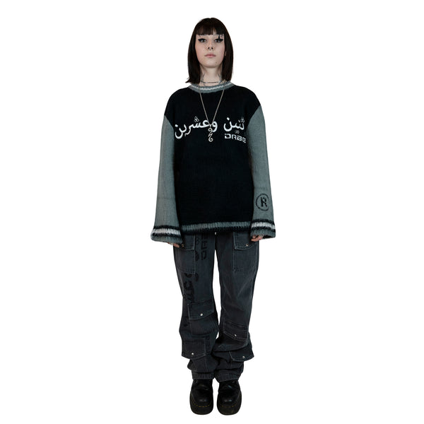 A pair of grey denim jeans with a long cut design and glitter print on the right leg. The jeans feature custom button and rivets, six usable pockets at the front, and an oversized unisex fit. Perfect for stacking on shoes for an on-trend look.