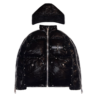 A black puffer jacket with a detachable hood, designed for streetwear enthusiasts. The jacket is made of 100% nylon shell and has 100% cotton down filling for warmth. It features custom DABE logo rivets and buttons, metallic hardware, and 22 custom pullers for added style. Both sleeves can be zipped for arm movement and there is a logo tape at the chest.