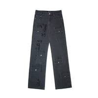 A pair of grey denim jeans with a long cut design and glitter print on the right leg. The jeans feature custom button and rivets, six usable pockets at the front, and an oversized unisex fit. Perfect for stacking on shoes for an on-trend look.